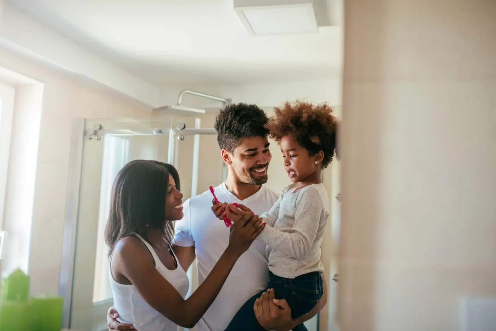 Parents helping their young daughter brush her teeth at home